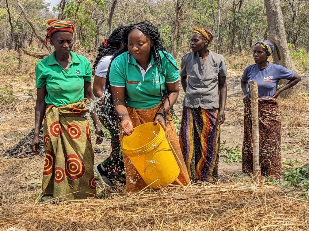 Women working together in a field, carrying a yellow container